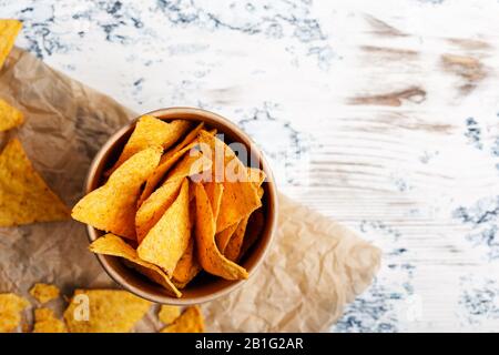 Tortilla-Chips in handwerklicher Papierschüssel auf rustikalem Holztisch von oben aus gesehen, aus der Nähe Stockfoto