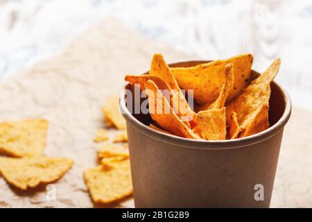 Tortilla-Chips in handwerklicher Papierschüssel auf rustikalem Holztisch, Nahaufnahme Stockfoto