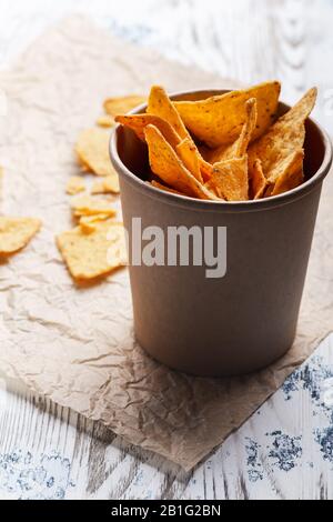 Tortilla-Chips in handwerklicher Papierschüssel auf rustikalem Holztisch, Nahaufnahme Stockfoto