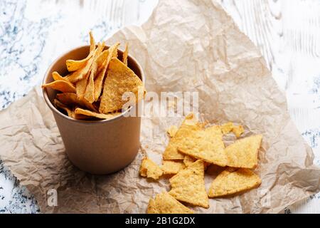 Tortilla-Chips in handwerklicher Papierschüssel auf rustikalem Holztisch, Nahaufnahme Stockfoto