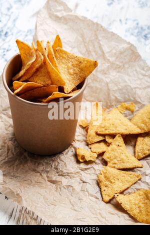 Tortilla-Chips in handwerklicher Papierschüssel auf rustikalem Holztisch, Nahaufnahme Stockfoto