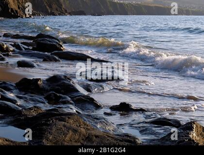 Farbfoto der Küstenfelsen am Strand einige geglättet und abgerundet durch die Passagen von Zeit und Flut mit Steinkobbeln und Kieselsteinen, die auf t liegen Stockfoto