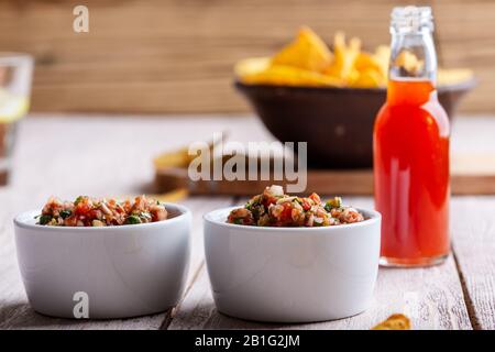 Zwei Schüsseln voller Salsa-Bad, heiße rote Chilisauce Flasche und Tortilla-Chips auf rustikalem Holztisch Stockfoto