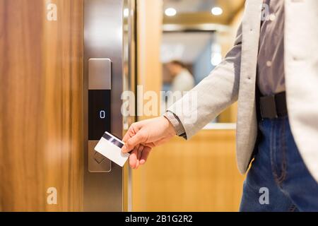 Mann, der die Schlüsselkarte am Sensor hält, um die Aufzugstür in einem modernen Gebäude oder Hotel zu öffnen.