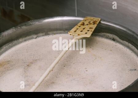 Ein langer Kunststoffrührer zum Rühren von Speisen in einer großen Pfanne. Bierbrauen. Die Technologie der Bierherstellung Stockfoto