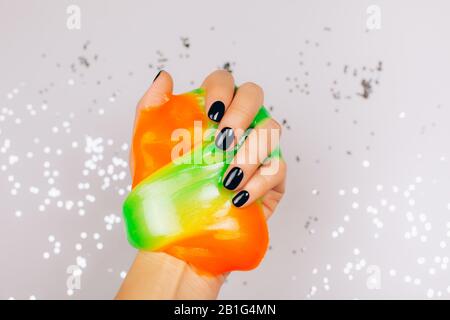 Hände mit schwarzer Maniküre, die Schleim in orange und grün leuchtenden Farben hält Stockfoto