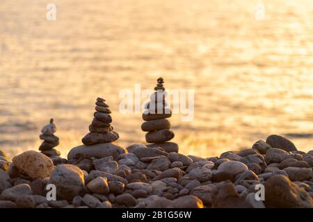 Balancierte Steinpyramide am Ufer des Ozeans im Morgengrauen. Der Turm mit Meeresschälchen steht für Stabilität, Zen, Harmonie und Gleichgewicht. Stockfoto