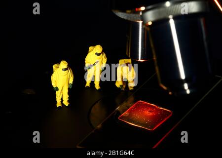 Konzeptionelles Bild von Miniaturfigurenmenschen, die Hazmatanzüge tragen und unter einem Mikroskop eine Probe von gefälschtem Blut betrachten Stockfoto