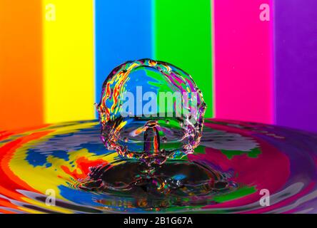 Abstraktes Foto einer Wasserfallenkollision, die durch zwei Wassertropfen entstanden ist, die isoliert vor einem farbenfrohen Hintergrund zusammenspritzen. Stockfoto