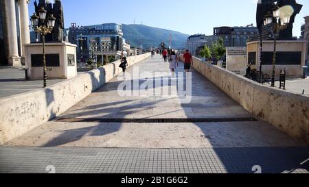 Skopje, Nord-Mazedonien, 27. Juni 2019: Menschen, die über die Steinbrücke spazieren, Denkmal Alexanders des Großen und Fahne Mazedoniens am Ende der Brücke Stockfoto