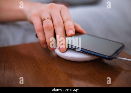 Frau händige Nahaufnahme, indem sie das Telefon auf ein drahtloses Ladegerät aufsetzt Stockfoto