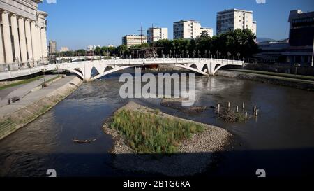 Skopje, Nord-Mazedonien, 27. Juni 2019: Niedriger Wasserstand des Flusses Vardar enthüllen kleine Insel mit Laub im Sommer mit Brücke auf dem zentralen Platz Stockfoto