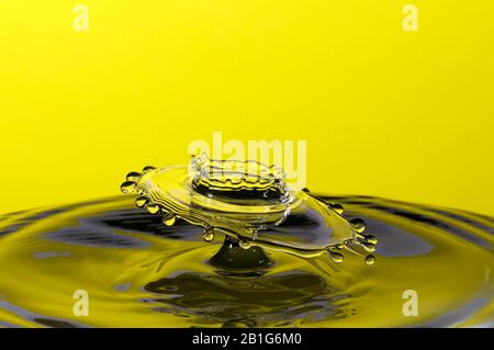 Abstraktes Foto einer Wasserfallenkollision, die durch zwei Wassertropfen entstanden ist, die isoliert vor einem gelben Hintergrund zusammenspritzen. Stockfoto