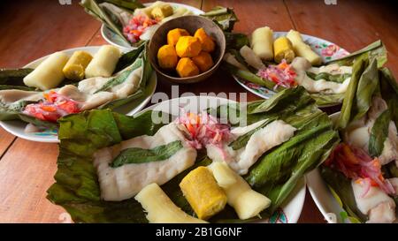 Gerichte mit Fisch Maitos, typische Gerichte des ecuadorianischen Amazonas, begleitet von Maniok, gekochten Bananen und Salat auf einem Holztisch Stockfoto