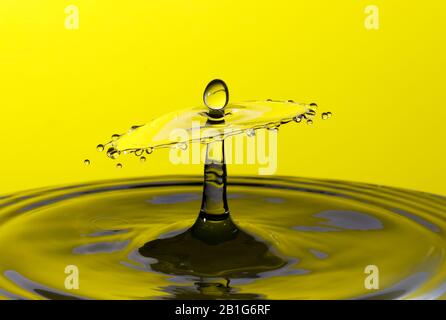 Abstraktes Foto einer Wasserfallenkollision, die durch zwei Wassertropfen entstanden ist, die isoliert vor einem gelben Hintergrund zusammenspritzen. Stockfoto