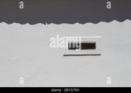 Weiße Fassade eines Gebäudes, durch das Sonnenlicht aufgeklärt. Schatten der Dachkante nach oben. Lüftungsabstand mit weißem Rahmen. Estoi, Portugal. Stockfoto