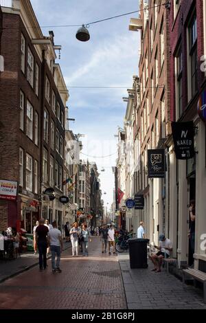 Blick auf die Leute, die auf der Warmoesstraat Straße in Amsterdam spazieren gehen. Es ist eine der ältesten Straßen mit vielen Cafés, Restaurants und Geschäften. Es ist eine sonnige Summe Stockfoto