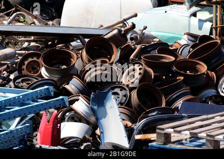 Haufen alter verrosteter Autofelgen gemischt mit verschiedenen anderen Autoteilen, die auf dem Schrottplatz vor Ort zum Recycling und zur Wiederverwendung bei anderen Autos zurückgelassen wurden Stockfoto