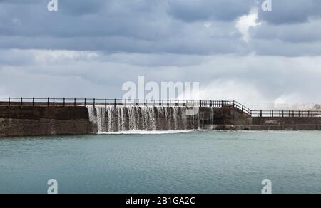 Stürmische Wellen gehen über Betonbruchwasser unter dunklem Himmel. Montazah Strand, Alexandria, Ägypten Stockfoto