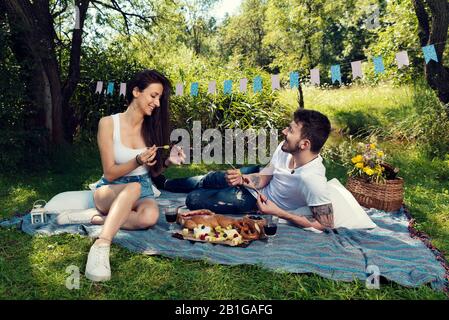 Junge Paare, die Picknick machen und Obstspieße auf einer Decke im Stadtpark Selective Focus sitzen Stockfoto