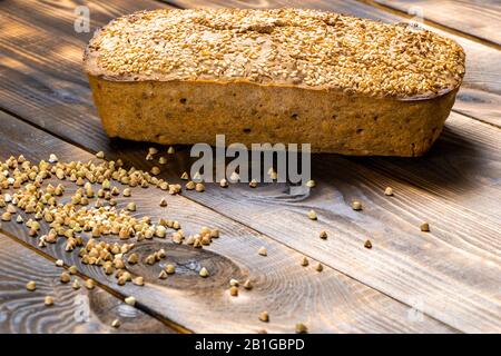 Glutenfreies Buchweizenbrot mit goldbrauner Kruste, bestreut mit Sesamsamen, liegt auf einem Holztisch. Gesundes hausgemachtes Rezept. Körner von Grün Stockfoto