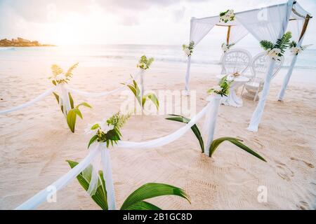 Dekorierte romantische Hochzeitsfeier mit Tisch und Stühlen am tropischen sandigen Strand in Sonnenuntergang, Seychellen Inseln Stockfoto