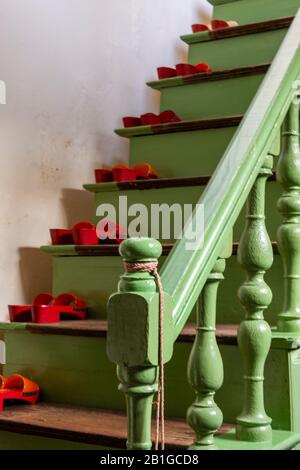 Eine grün bemalte, altmodische Holztreppe mit Bannister und Neupfosten mit Paar Schuhen, die sich auf der Treppe befinden. Stockfoto