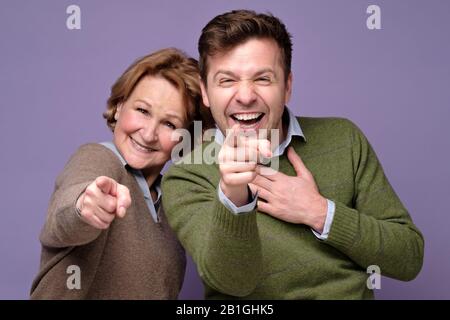 Mutter und Sohn des mittleren Alters lachen über Sie und zeigen mit dem Finger auf die Kamera. Großer Witz. Positive menschliche Emotionen im Gesicht. Stockfoto