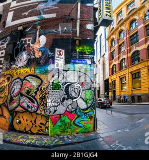 Totenkopfbemalung und verschiedene gemalte Designs, Graffiti-bedeckte Trageband mit Familienuntergang im Hintergrund. Hosier Street, Melbourne Lan Stockfoto