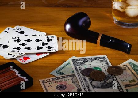 Glücksspiel - Rauchpipe, Spielkarten, Scotch Whiskey und US-Dollar-Banknoten auf dem Holztisch Stockfoto