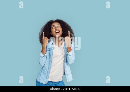 Freistil. Afrikanisches Mädchen, das isoliert auf Grau steht und lächelnd nach oben auf den Kopierraum zeigt Stockfoto