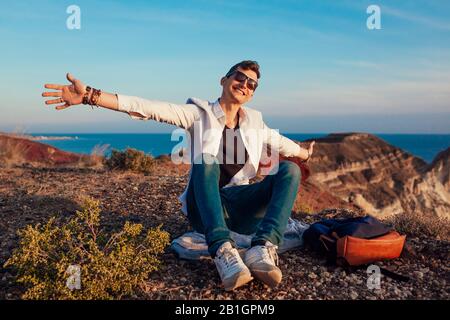 Touristen Wanderer, die auf der Bergkuppe am Meer auf der Insel Santorini Spaß haben und die Landschaft genießen. Glücklicher Mann öffnete die Arme auf Reisen Stockfoto