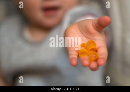 Das Kind kommt mit Pasta heraus. Das Kind bietet Essen an. Selektiver Fokus auf der Hand. Stockfoto