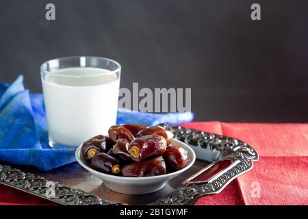 Datteln und ein Glas Milch auf Metallschale und bunte Servietten. Ramadan, Iftar Food Concept. Dunkler Hintergrund, Kopierbereich Stockfoto
