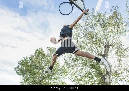 Basketballspieler, der auf dem Platz im urbanen Grunge Camp mit Rückenlicht große Slam-Dunk ausführt - Yong Athlet in Action Outdoor - Sport Concept - Origi Stockfoto