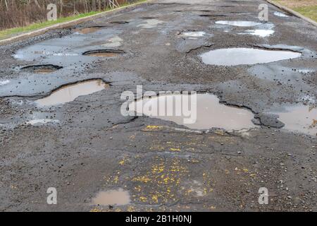 Eine gepflasterte Straße mit vielen großen Schlaglöchern, die Schlaglöcher sind mit Wasser gefüllt. Stockfoto