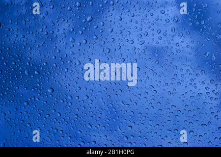 Viele Wassertropfen auf blauem Glas. Wolken im Hintergrund oben. Stockfoto