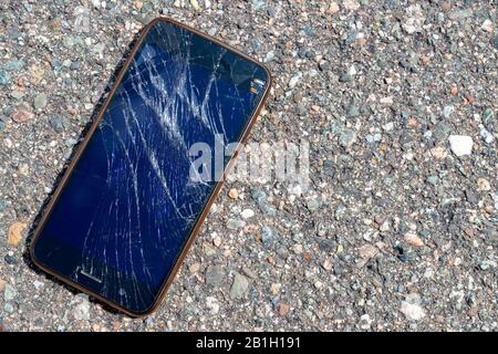 Ein zerbrochenes und zerbrochenes Handy, das auf einer Asphaltstraße liegt. Der Bildschirm auf dem Handy ist kaputt und zerbrochen. Das Telefon ist nicht identifizierbar. Stockfoto