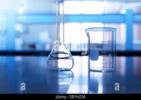 Becher und volumetrischer Kolben auf dem blauen Labortisch der Chemiewissenschaft Stockfoto