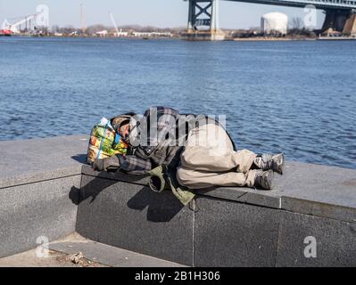 Philadelphia Pennsylvania, 23. Februar 2020: Ein obdachloser Mann schläft auf einer Steinbank entlang der Uferpromenade bei Penn's Landing Stockfoto