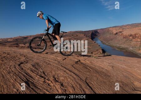 25. Februar 2020: Das Bureau of Land Management kündigte am 24. Februar an, zwei Parzellen innerhalb des Sand Flats Special Recreation Area in der Nähe von Moab, Utah, aus einem bevorstehenden Verkauf von Öl- und Gaspacht zu entfernen. Der Plan hätte Sondierungsbohrungen unter dem Slickrock Trail ermöglicht, einem der beliebtesten Mountainbike-Ziele der Welt. Bild: 5. April 2015 - Moab, Utah, USA - Mountain Biker TIM-SPUR, die den roten Sandstein des berühmten Slickrock-Trails mit Colorado River und Canyons hinter sich führt. Der Slickrock Trail ist ein beliebtes Mountainbike-Ziel mit weltweitem Ruhm. T Stockfoto