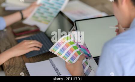 Ein zugeschnittenes Foto zweier junger Designer, die sich auf die Farbe der Farbfelder konzentrieren, während sie an einem Tablett auf einem Holztisch im gemeinsamen Arbeitsraum arbeiten Stockfoto