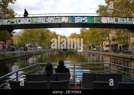 Passagiere auf einem Ausflugsboot mit einer Eisenbrücke über den Canal Saint Martin im Hintergrund.Paris.France Stockfoto