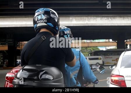 Quezon City, Philippinen - 17. Februar 2020: Motorradtaxifahrer und sein Passagier warten auf grünes Licht an einer Kreuzung einer belebten Straße. Stockfoto