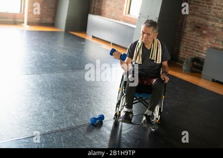 Älterer Mann im Rollstuhl, der eine Hantelübung macht Stockfoto