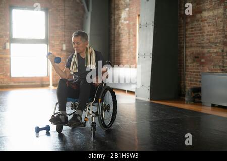 Älterer Mann im Rollstuhl, der eine Hantelübung macht Stockfoto