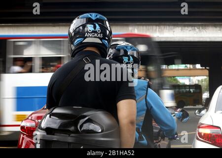 Quezon City, Philippinen - 17. Februar 2020: Motorradtaxifahrer und sein Passagier warten auf grünes Licht an einer Kreuzung einer belebten Straße. Stockfoto