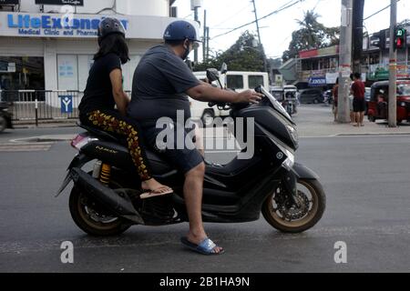 Quezon City, Philippinen - 17. Februar 2020: Motorradfahrer und sein Beifahrer warten auf grünes Licht an einer Kreuzung einer belebten Straße. Stockfoto