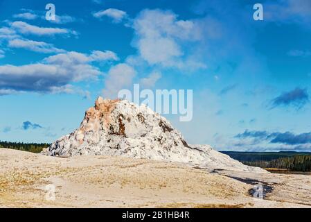Dampfende Geysir-Felsformation gegen einen blauen Himmel mit weißen Wolken.
