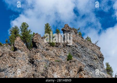 Blick auf hohe felsige Bergseite mit grünen Pinien auf der Oberseite unter blauem Himmel mit weißen flauschigen Wolken. Gefühl frei! Stockfoto